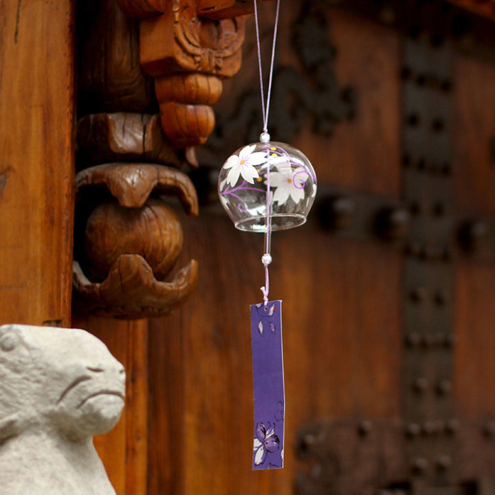 Glass Japanese wind chime with white flowers on wood, outdoor decor.