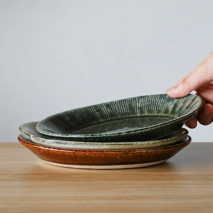 Nishida Muyu oval deep plate stack: forest green, earth brown ceramic sushi dishes on wooden table.