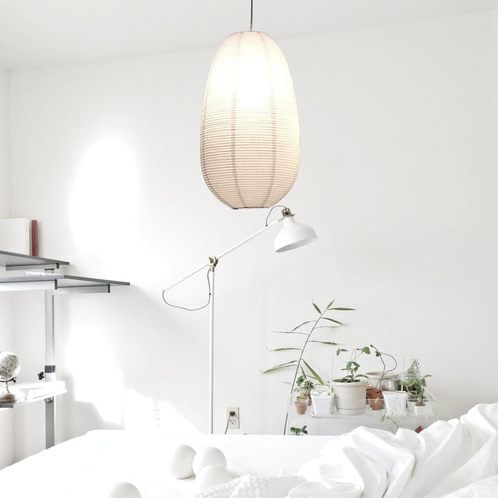 Oval paper lampshade hanging in a minimalist white room with plants and a floor lamp.