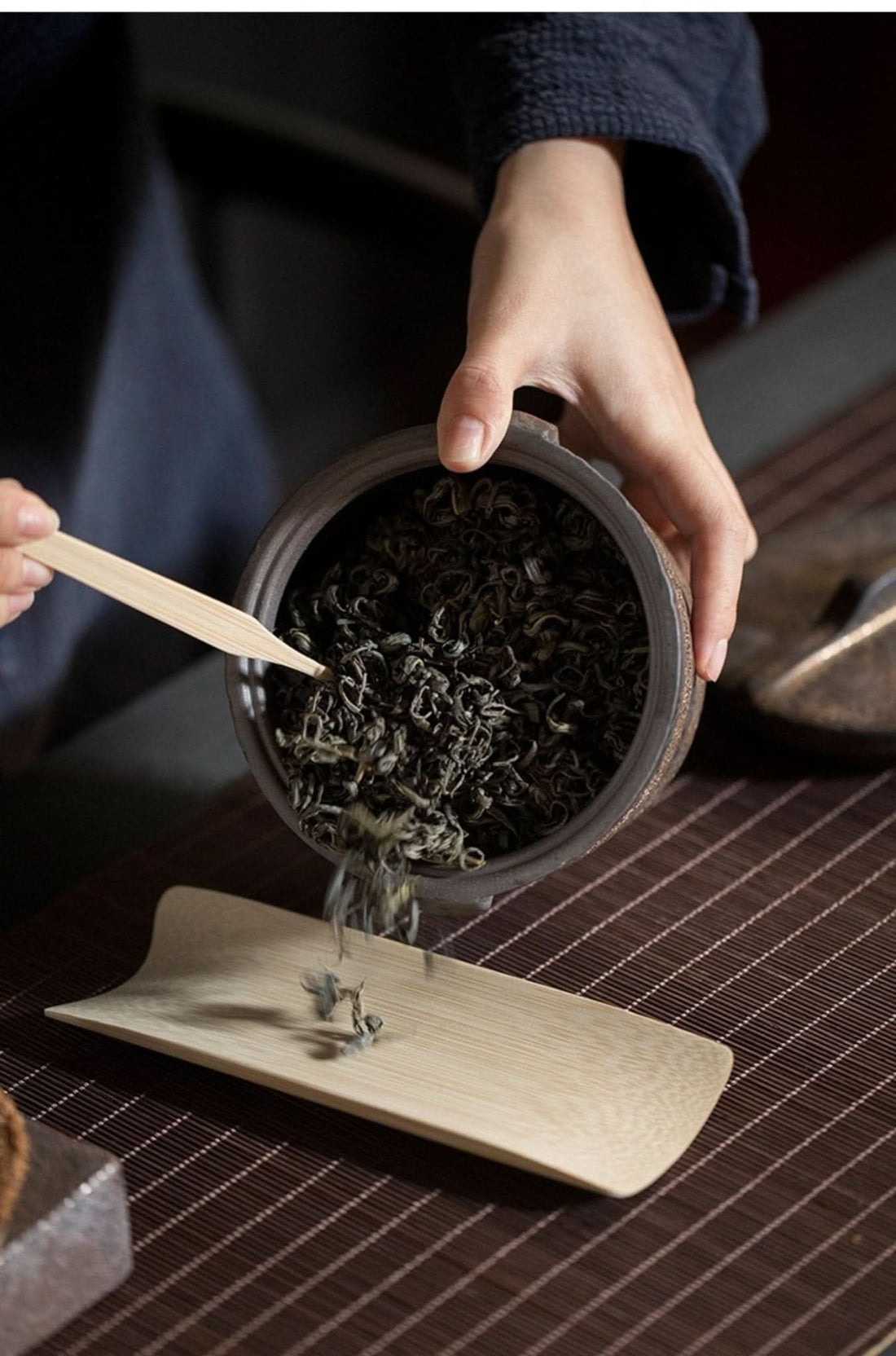 Vintage pottery Japanese tea jar pouring loose leaf tea onto bamboo scoop.