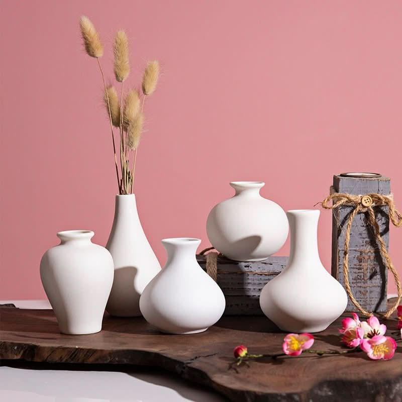 Small ceramic white bud vases with dried florals on a rustic wood surface.