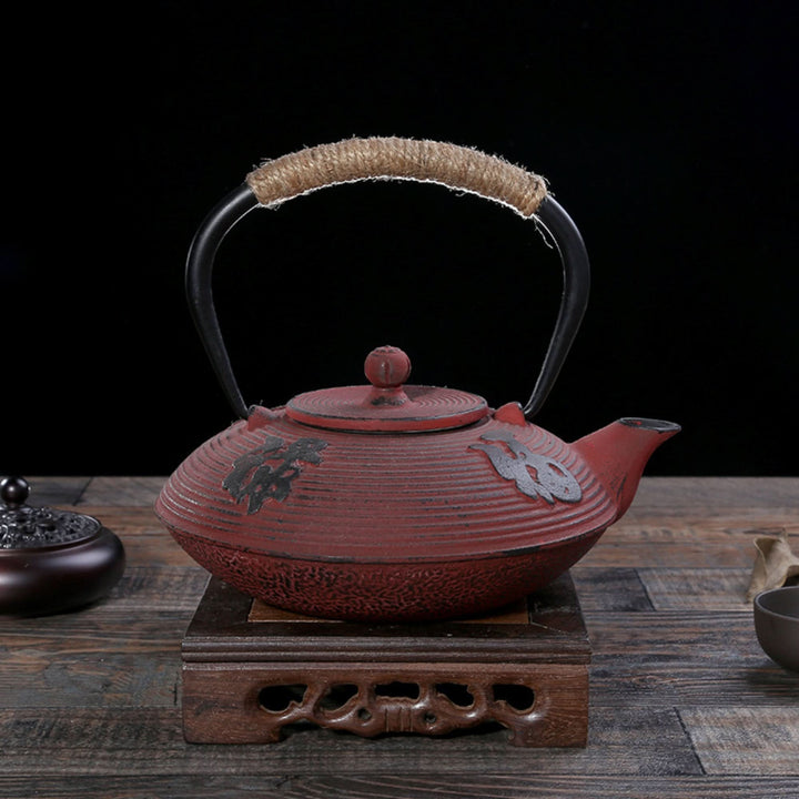 Red cast iron tea kettle with jute handle on wooden stand, decorative home decor.