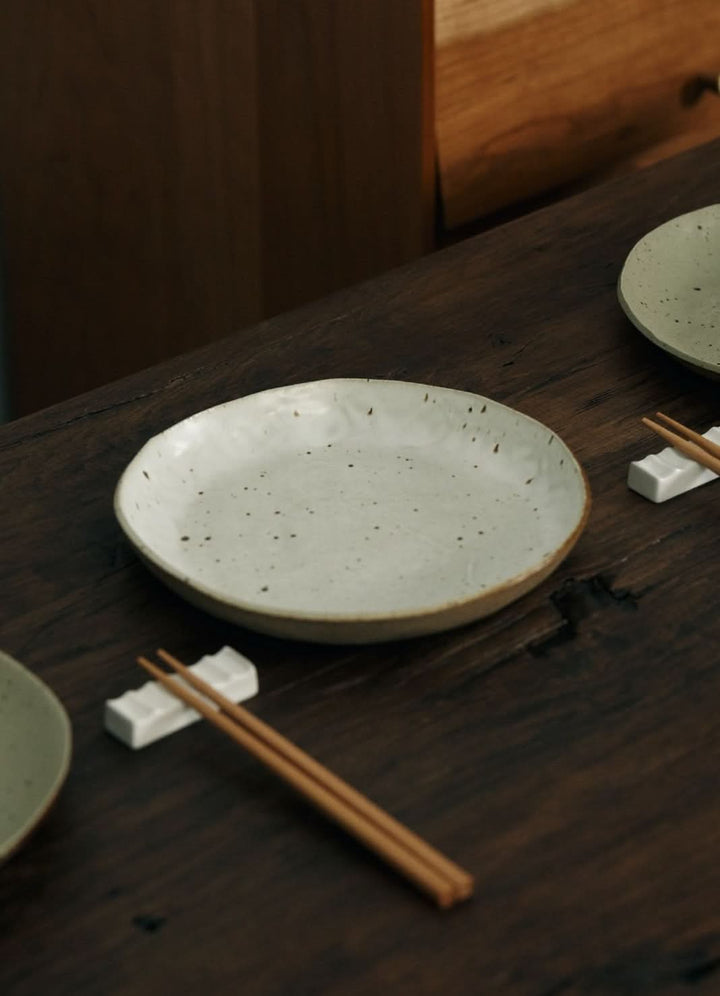 Handmade unglazed earthenware dinner plates with speckled design on rustic wooden table.