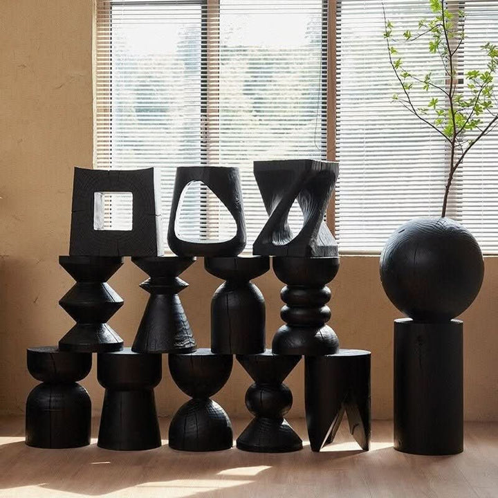 Various black wood stools with unique designs, including abstract and geometric shapes, displayed indoors.