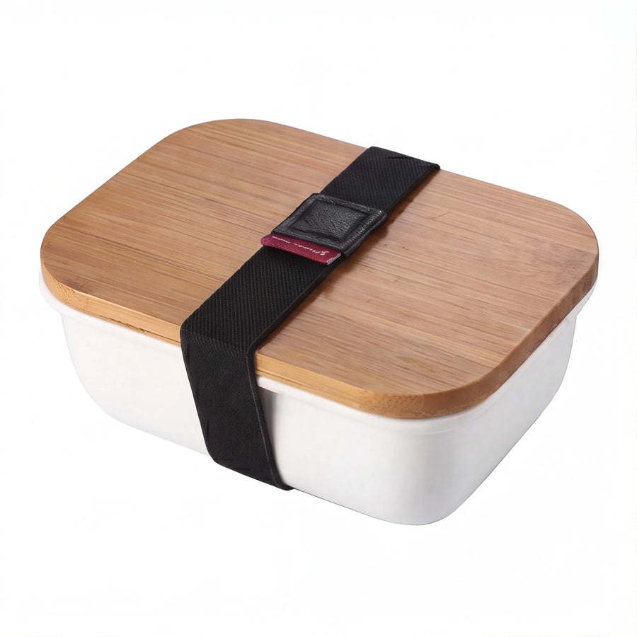 White ceramic bento box with bamboo lid and black elastic strap on white background
