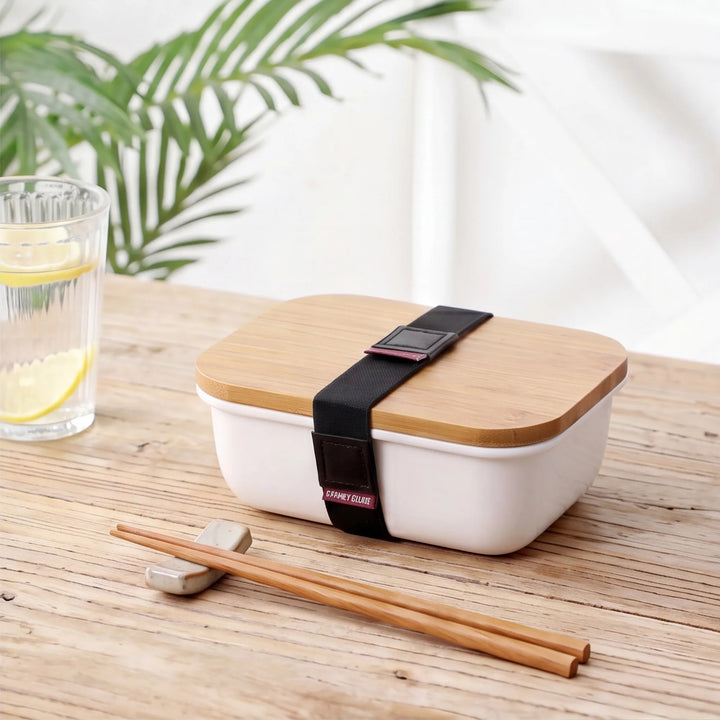 Ceramic bento box with wooden lid on dining table with chopsticks and lemon water in Japandi kitchen setting