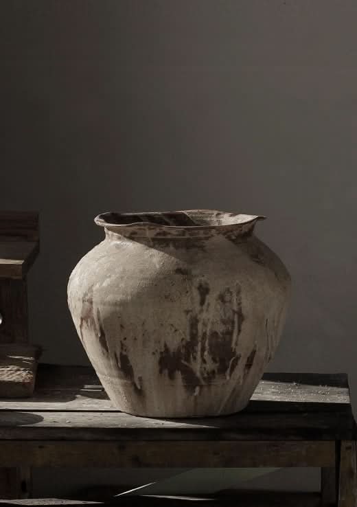 Large, rustic beige handmade ceramic vase with textured drips on distressed wooden surface.