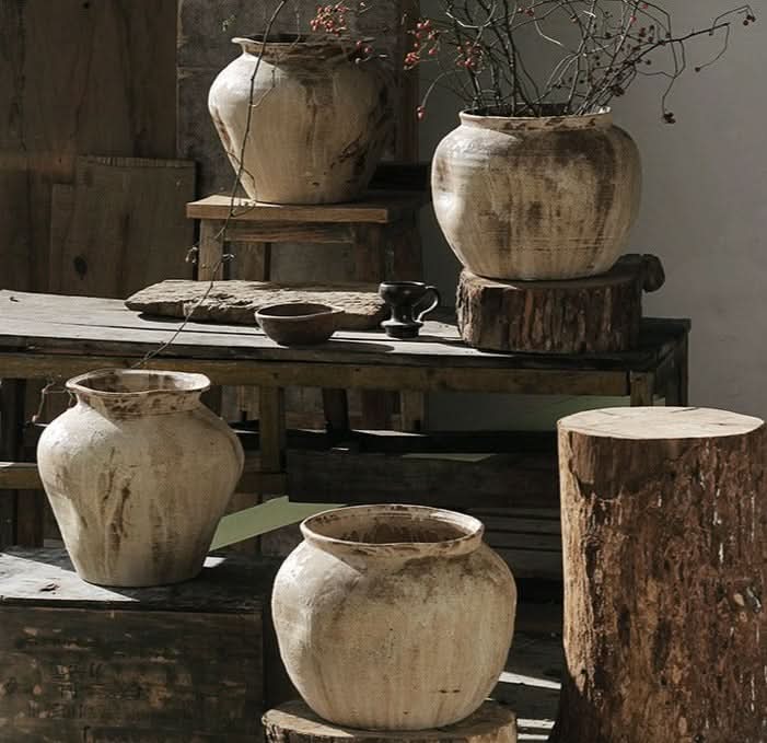 Rustic handmade ceramic vases in beige and brown tones, displayed on weathered wood.