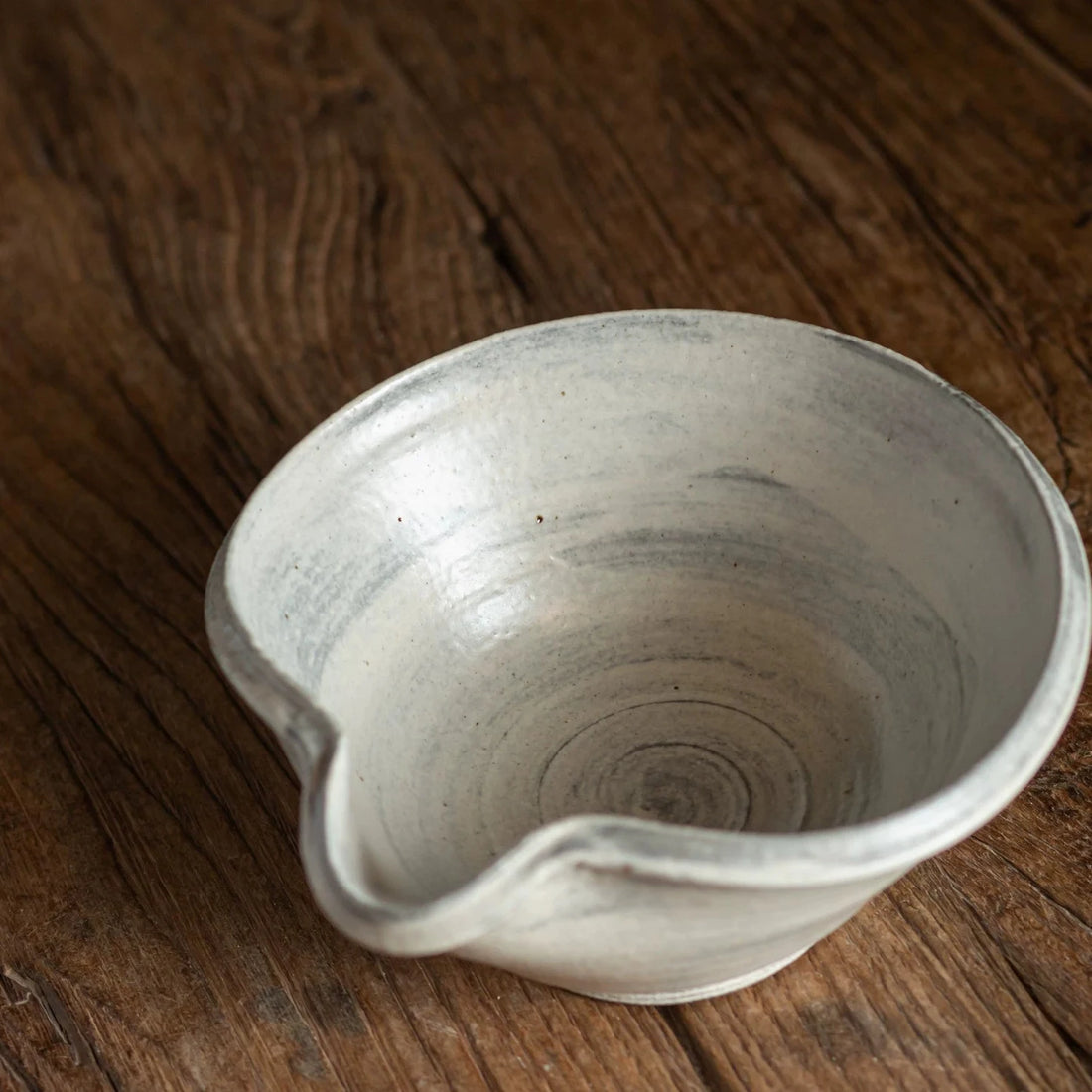 Overhead view of a light grey ceramic tea bowl with a distinct pouring spout and visible swirling pattern inside.