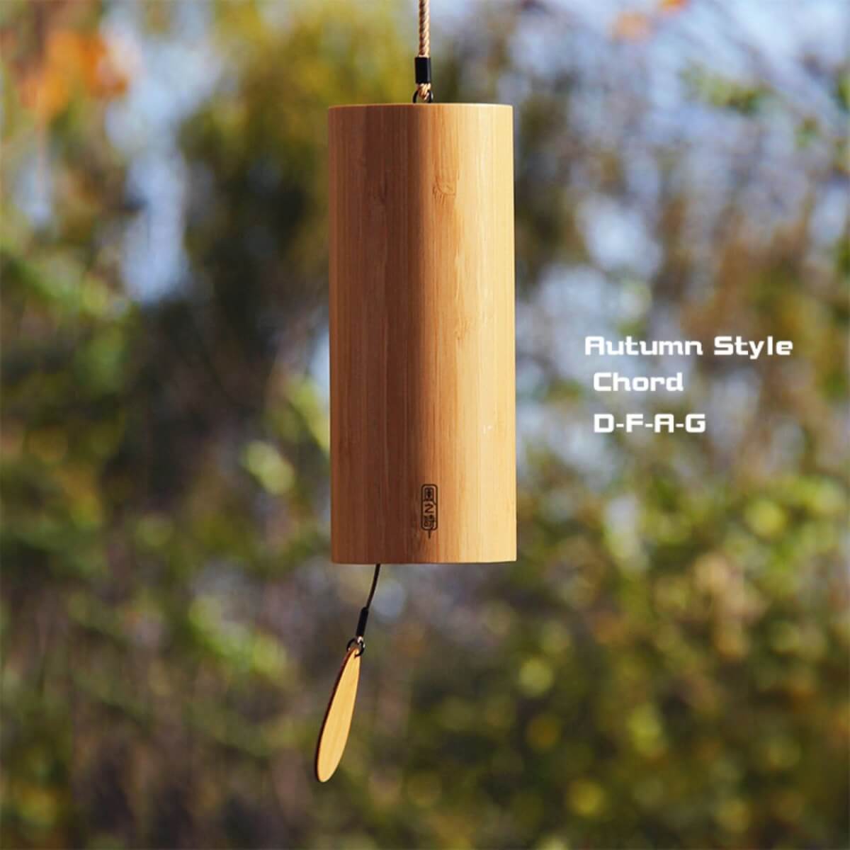Bamboo wind chime in natural wood tone, hung outdoors with a blurred green background. Autumn melody.