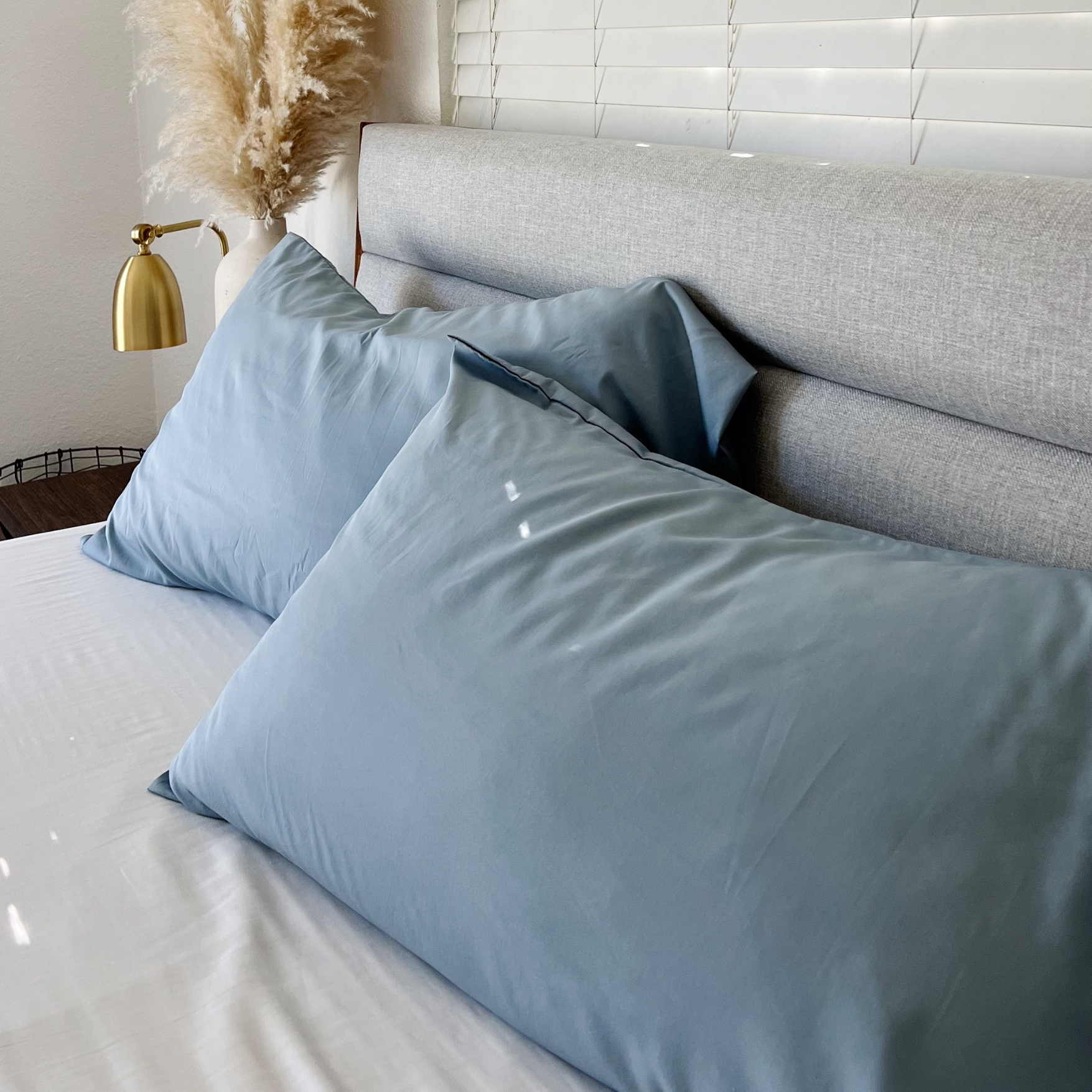 Light blue Copper Infused Bamboo Pillowcase Set on a bed with a grey headboard and white sheets.