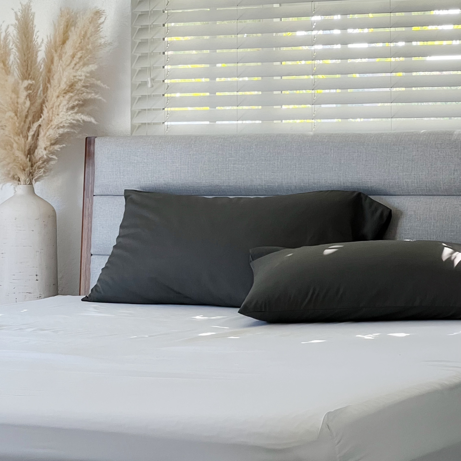 Dark grey Copper Infused Bamboo Pillowcase Set on a bed with blinds and pampas grass.