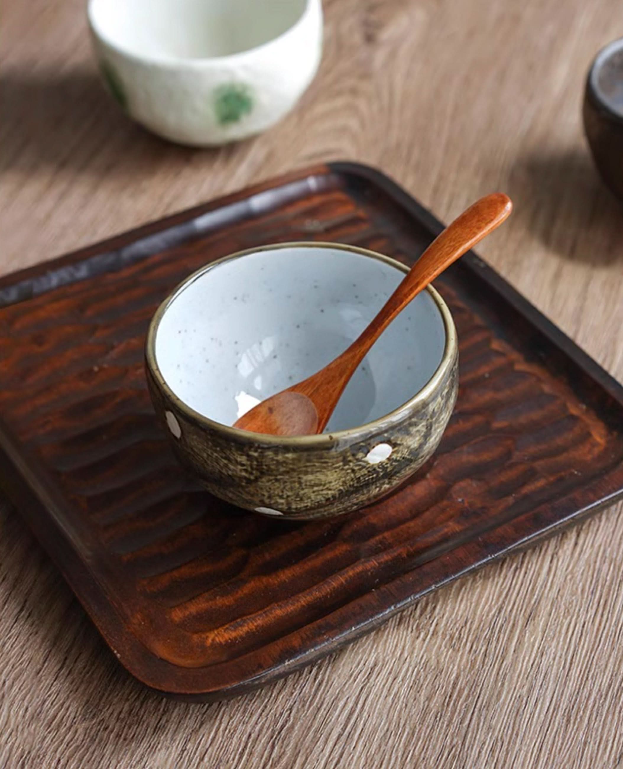 Mino-yaki wedge-shaped matcha bowl with wooden spoon on textured dark wood tray.