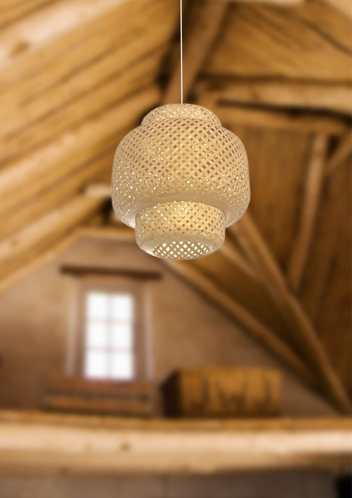 Woven bamboo pendant light with intricate pattern, natural color, hanging in a rustic attic setting.