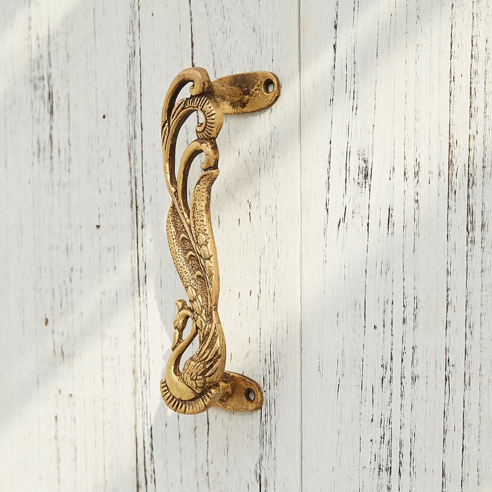 Ornate brass Phoenix Double Door Handle, handmade, on white wood.
