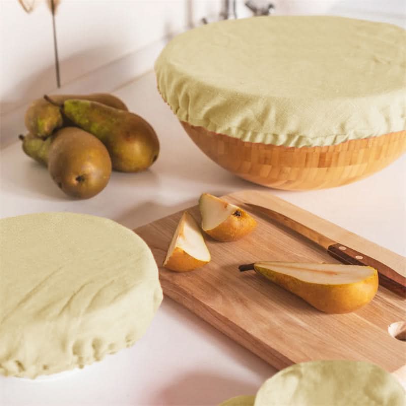 Light yellow linen bowl covers protecting bowls and pears on a countertop.