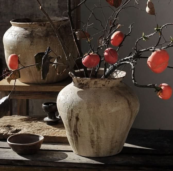 Two rustic handmade ceramic vases with branches of orange fruit, complementing home decor.