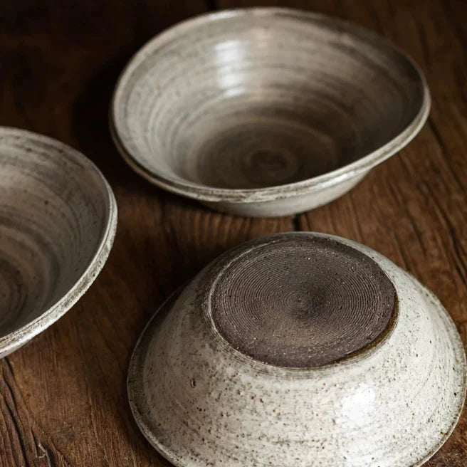 Three rustic ceramic bowls displayed, one flipped to show the textured base, on wood.