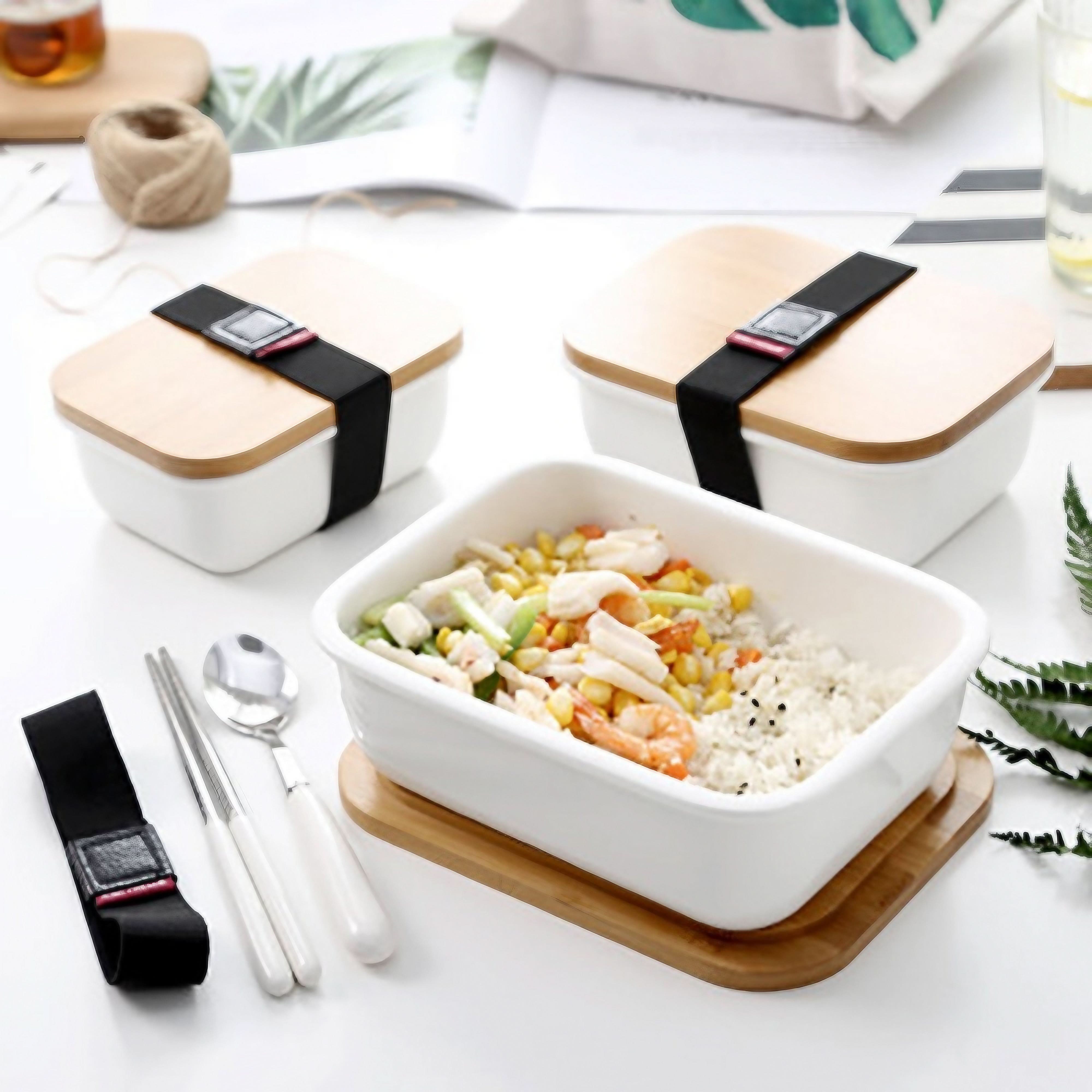 White ceramic bento box with bamboo lid and black strap, filled with rice and shrimp.