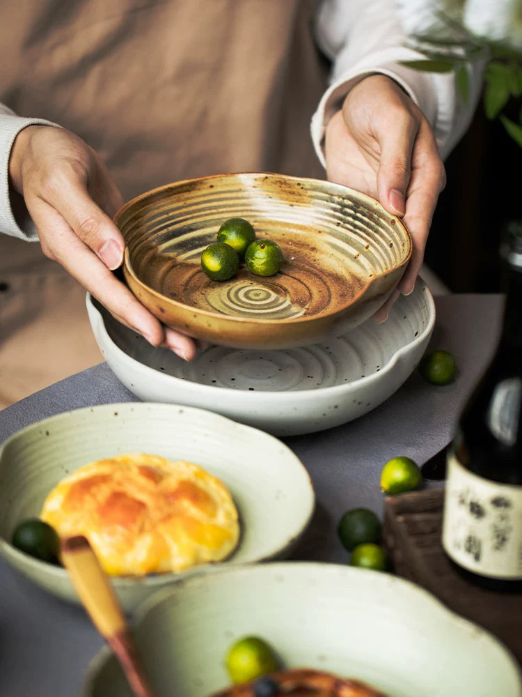 Hands holding small, swirl-patterned brown and white ceramic bowl with kumquats over other dishes.