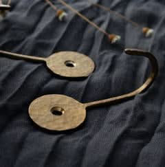 Hammered brass wall hook with textured finish on dark fabric background.