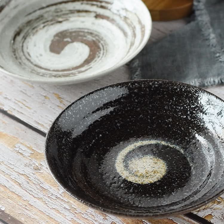 Two Japanese Pottery Tableware 9" bowls, one black, one white, with spiral designs on a wooden table.