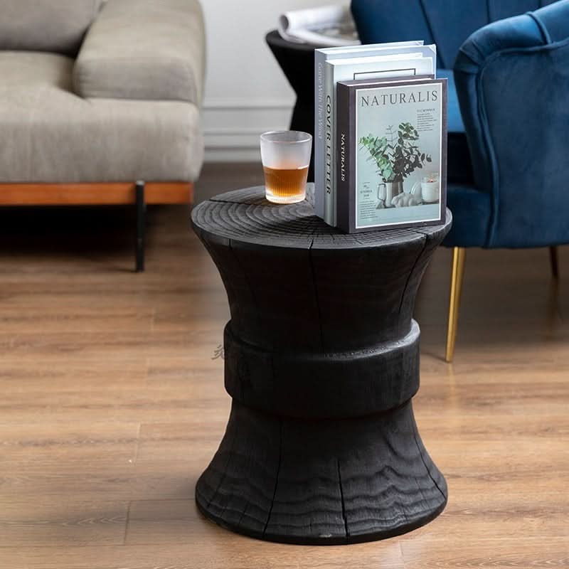 Black wood stool with rustic texture, holding books and a drink in a modern living room.