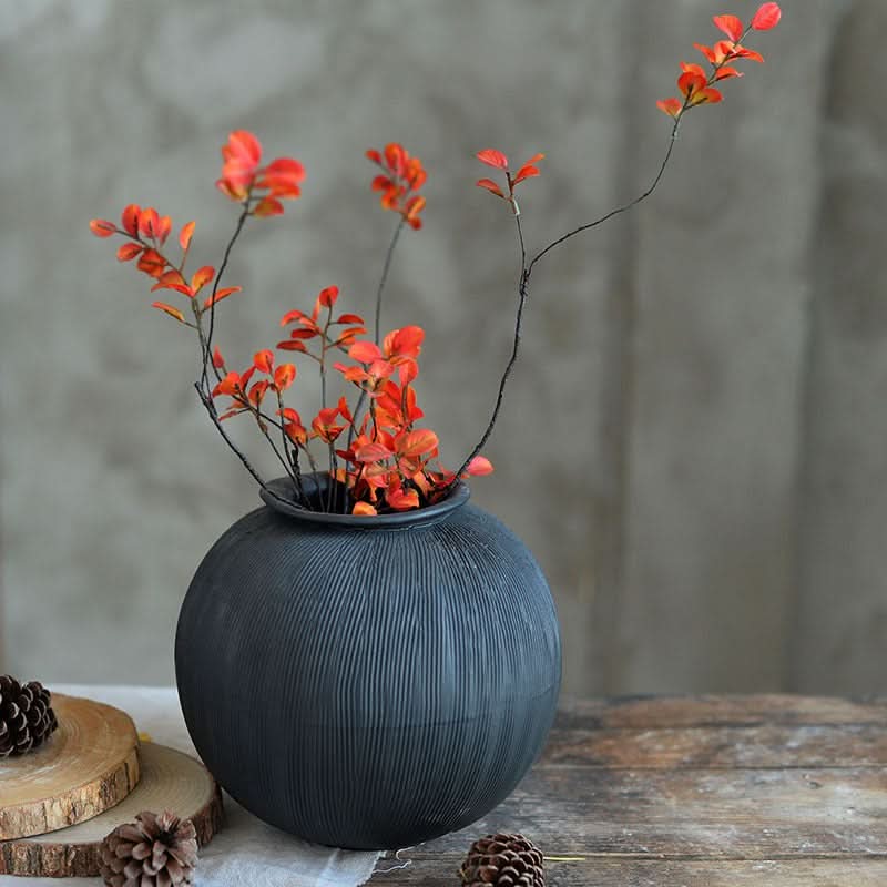 Textured black ceramic vase with orange branches on rustic wooden surface.