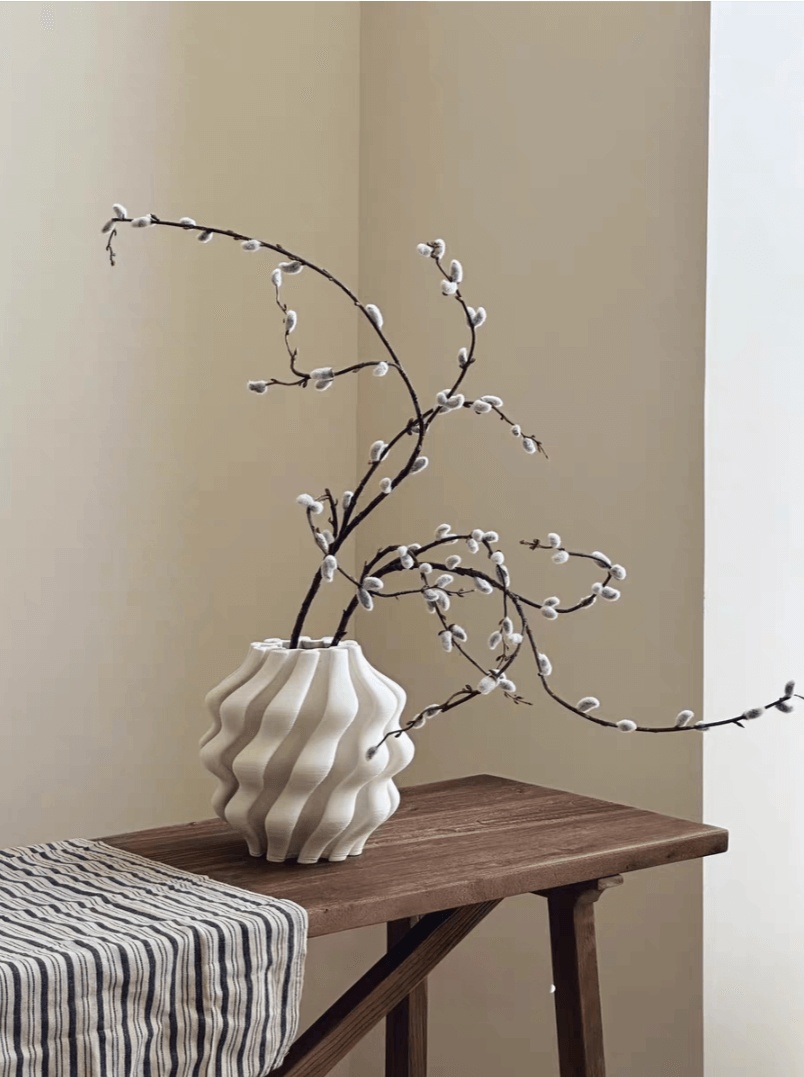 White 3D printed vase for plants with pussy willow branches on a wooden table.