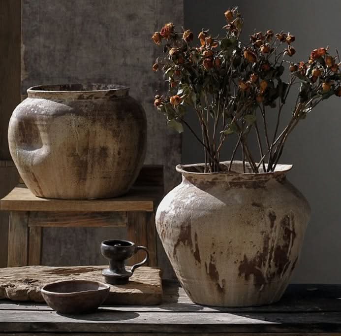Two handmade ceramic vases in rustic brown and beige tones, one with dried flowers.