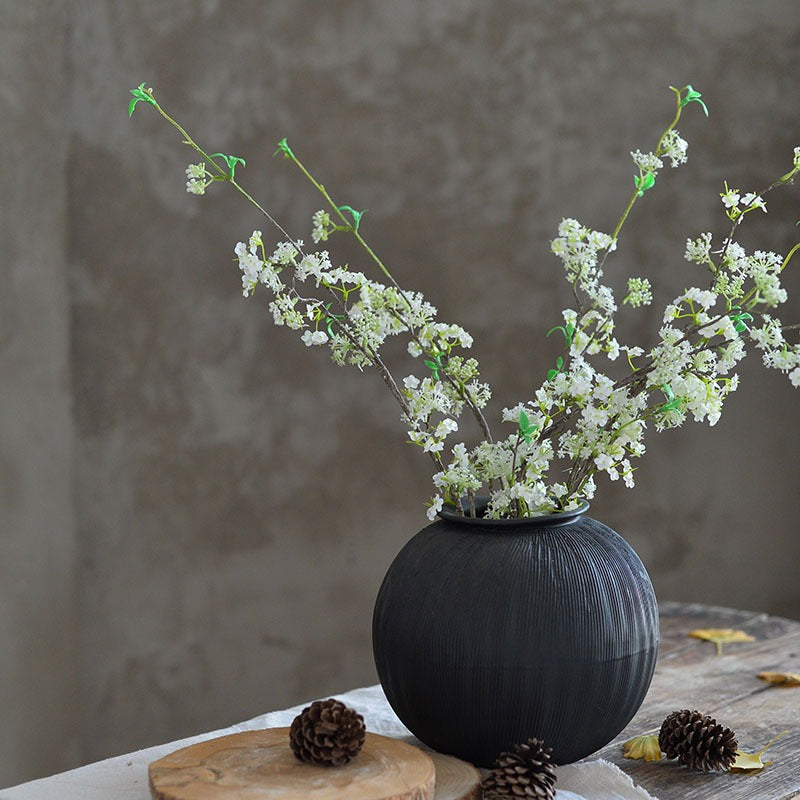 Black ceramic vase with textured surface, holding a white flower arrangement.