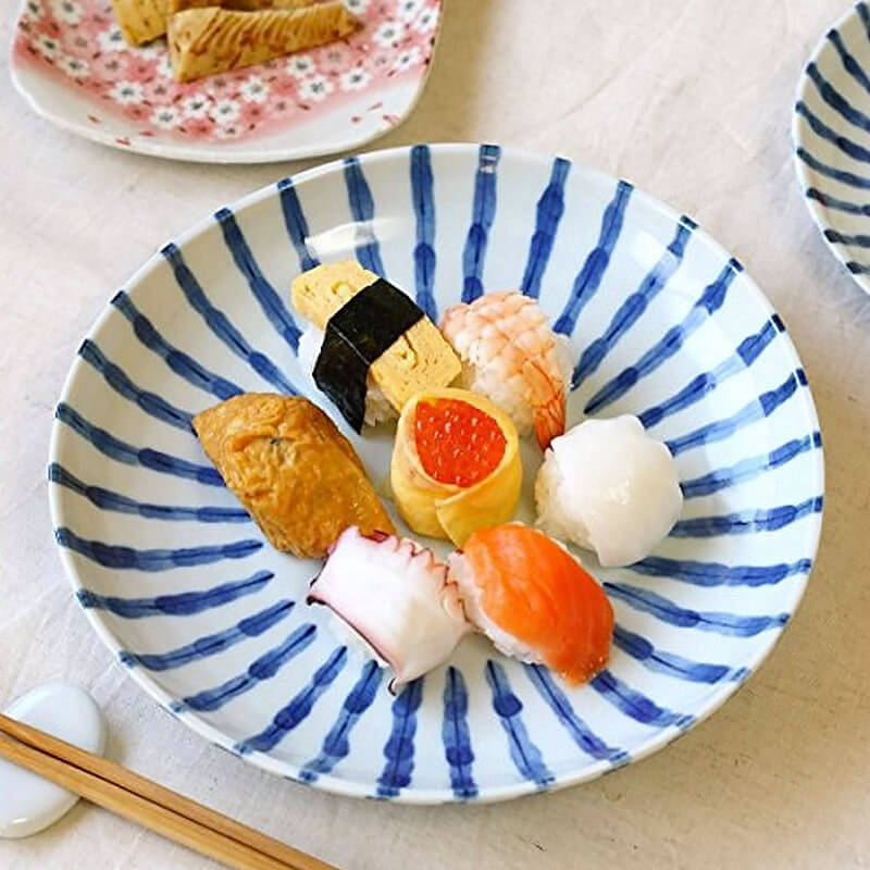 Blue and white plates made in Japan holding assorted sushi with chopsticks and a dipping sauce dish.