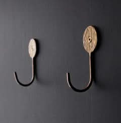 Hammered brass wall hook with textured face, mounted on dark wall.