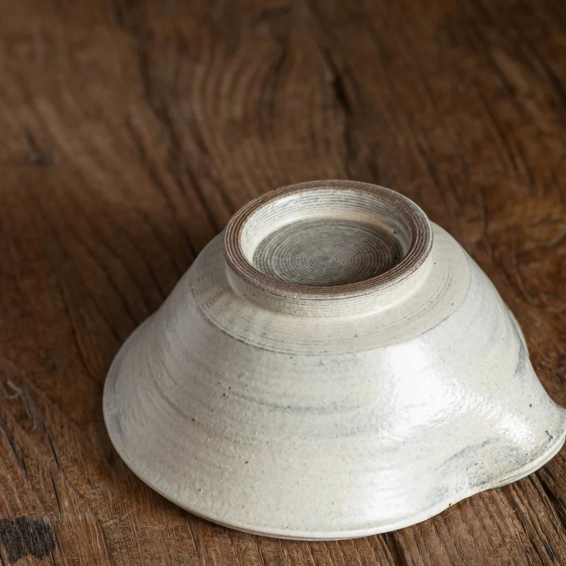 View of the bottom of a rustic ceramic bowl, showing the small, rough foot ring and the uneven body shape.