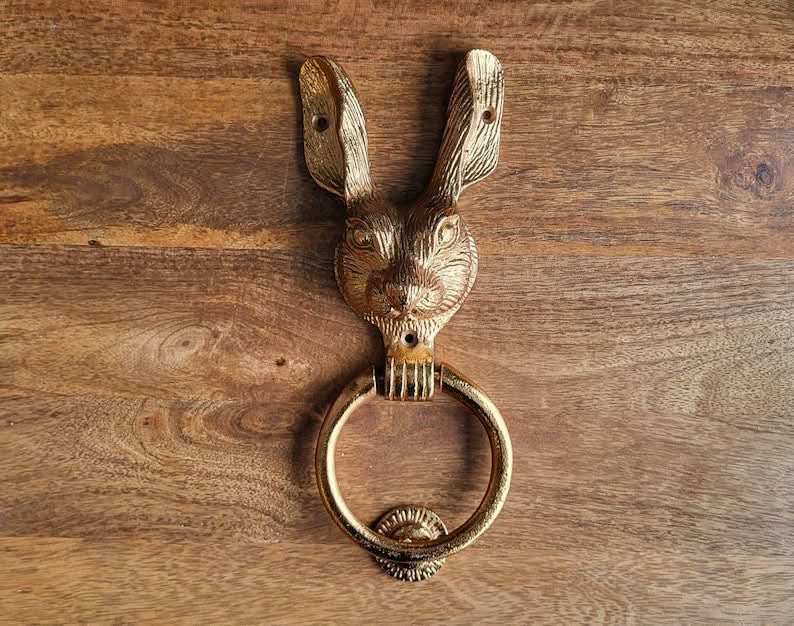 Golden brass rabbit door knocker on a wooden surface.