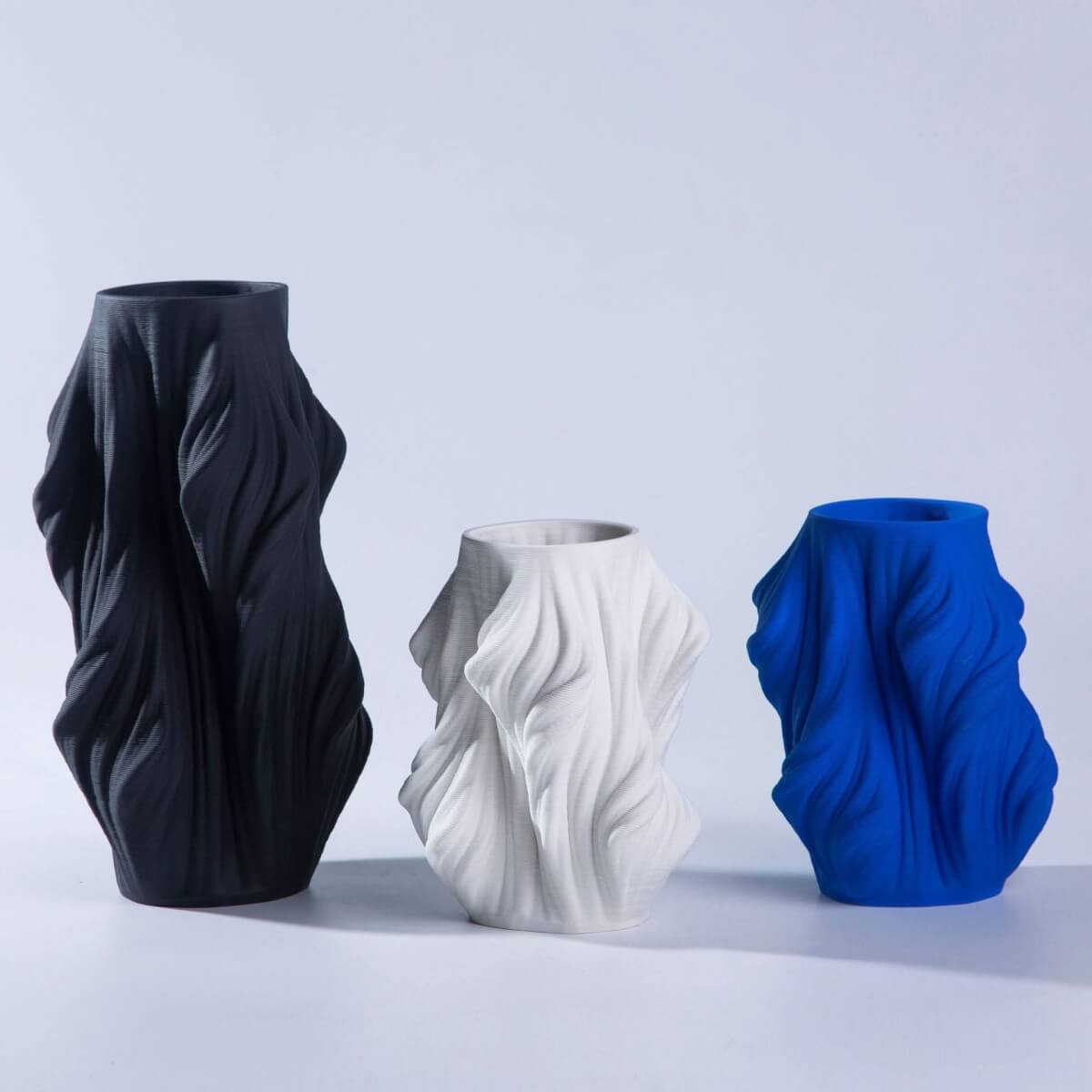 3D Printed Vase Made of Ceramic: Black, white, and blue draped vases on a white surface.