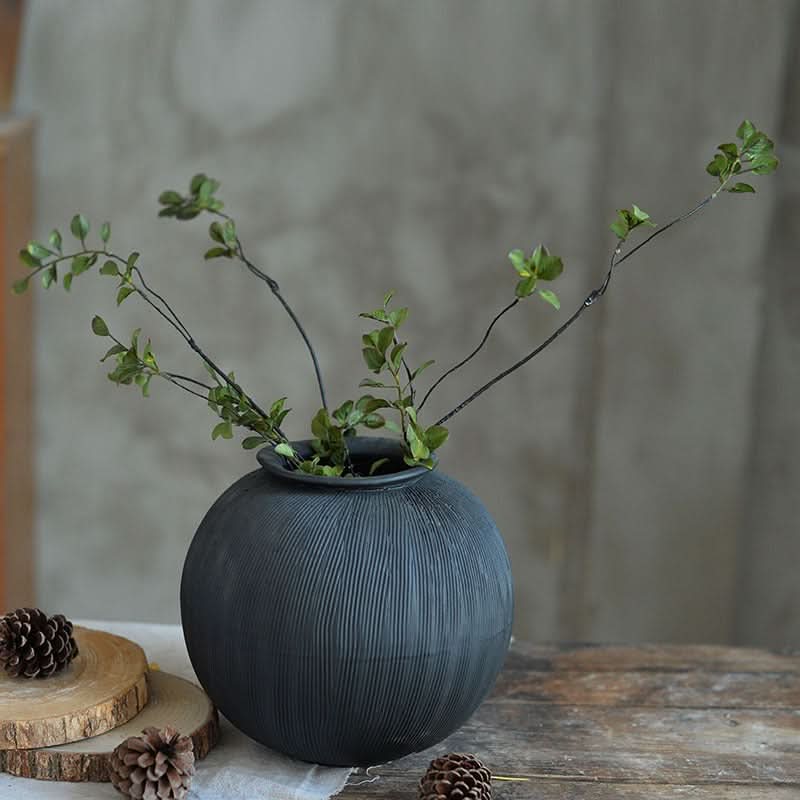 Textured black ceramic vase with green branches, displayed on a wooden table.