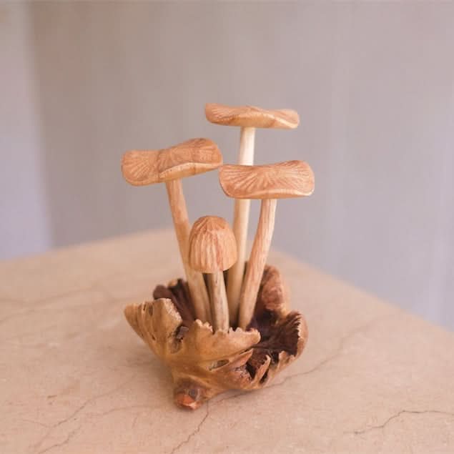Hand-carved wooden mushroom sculpture in natural tones on a textured surface.