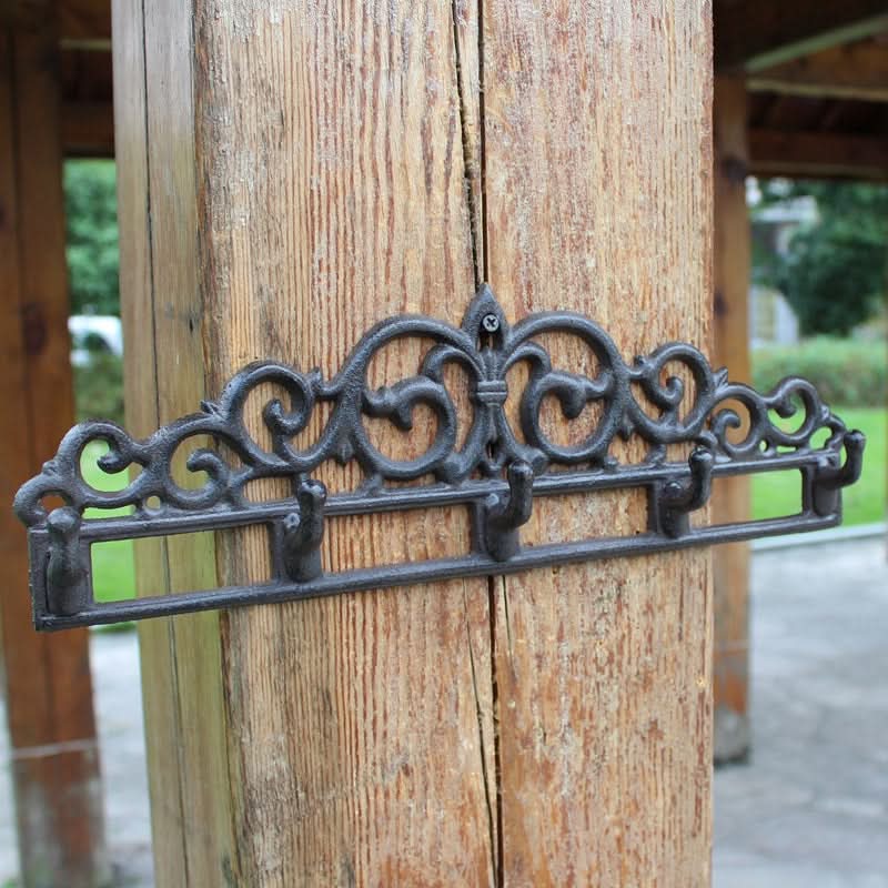 Ornate black cast iron outdoor wall hanger with 5 hooks mounted on a wooden post.