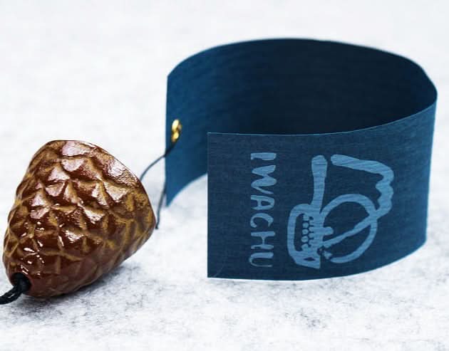 Brown pine cone wind chime with dark blue tag on textured surface