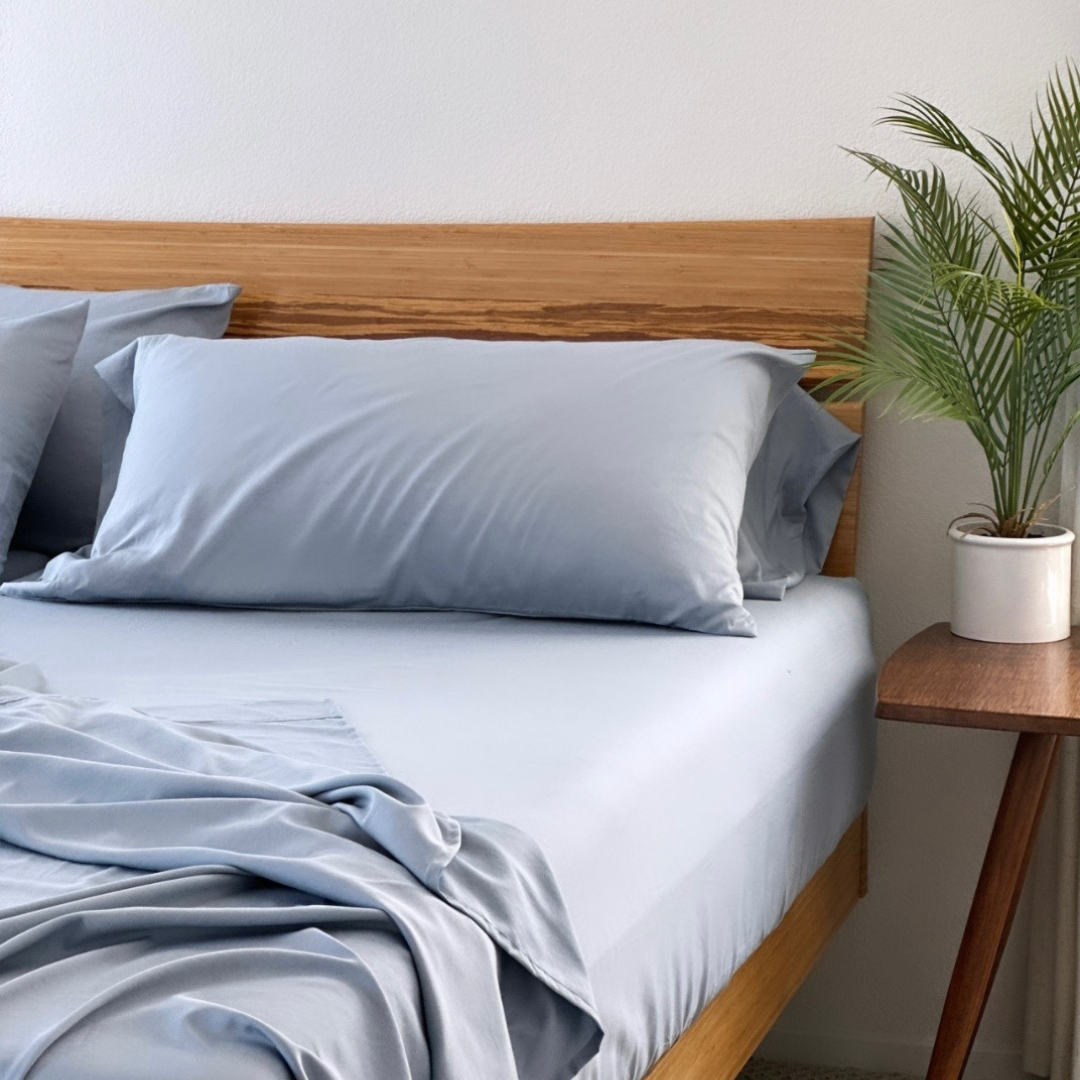 Light blue Copper Infused Bamboo Pillowcase Set on a bed with a wooden headboard and side table.