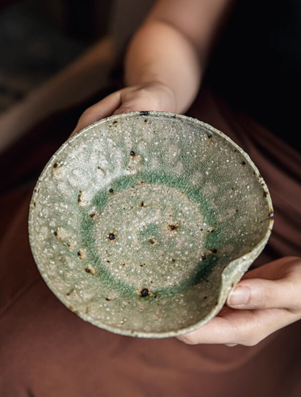 Artisan Green Dinnerware: Textured green ceramic bowl with rustic dark speckles, held by hands.