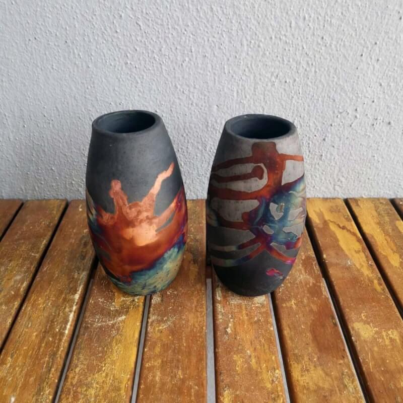 Two handmade ceramic vases, featuring a smoked raku finish with copper accents and unique designs.  Perfect for home decor.