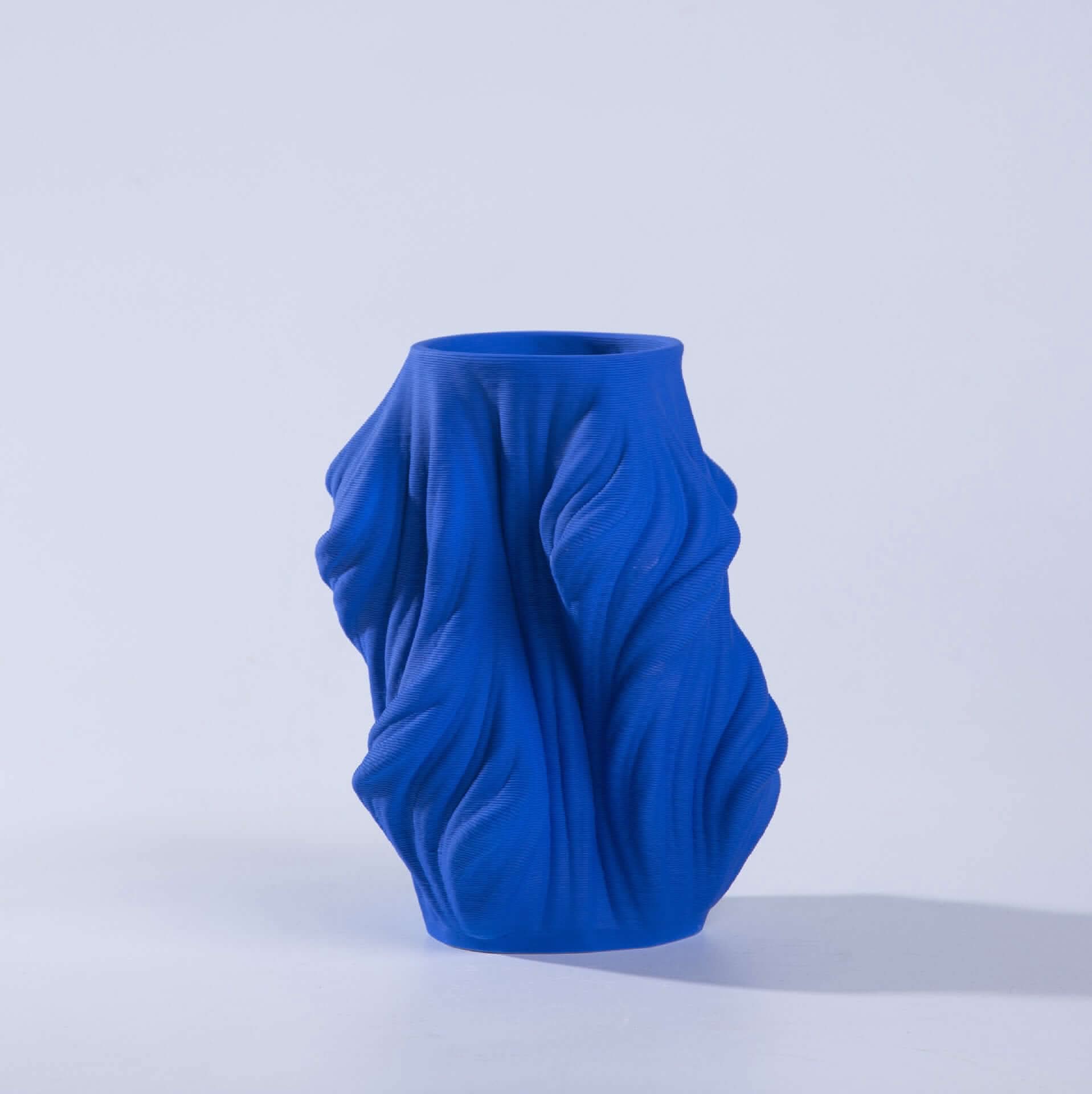 Bright blue 3D printed vase made of ceramic with a draped fabric effect on a white background.
