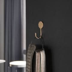 Hammered brass wall hook with textured finish holding a woven scarf against a dark wall.