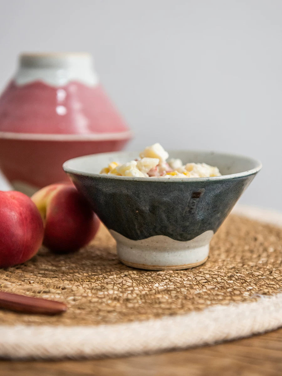 Ceramic bowl with dark blue/grey glaze filled with cereal, next to peaches.