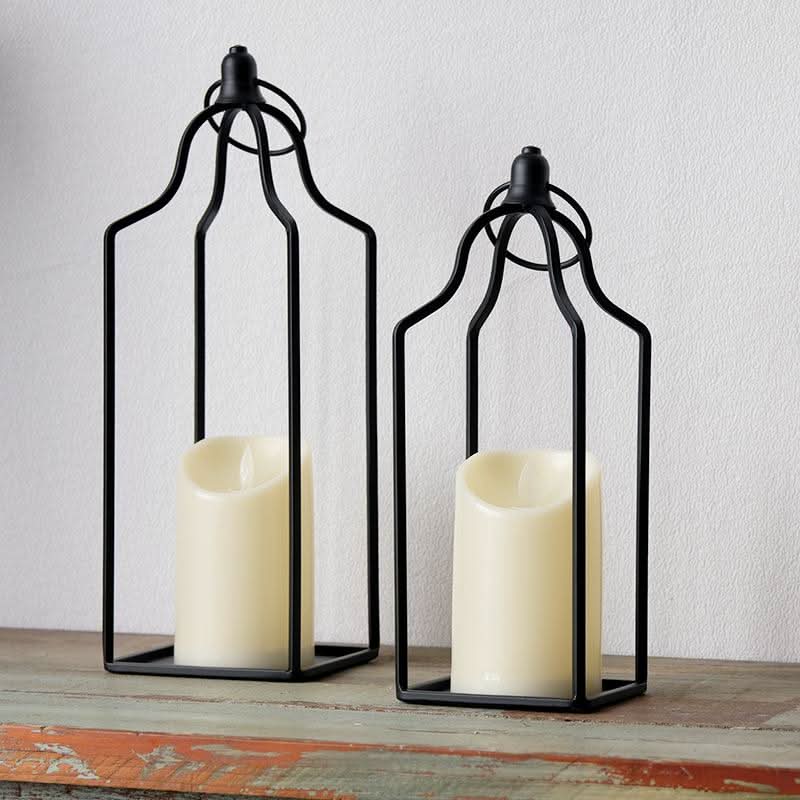Black metal line candle holder set of 2 with cream candles on a wooden surface.