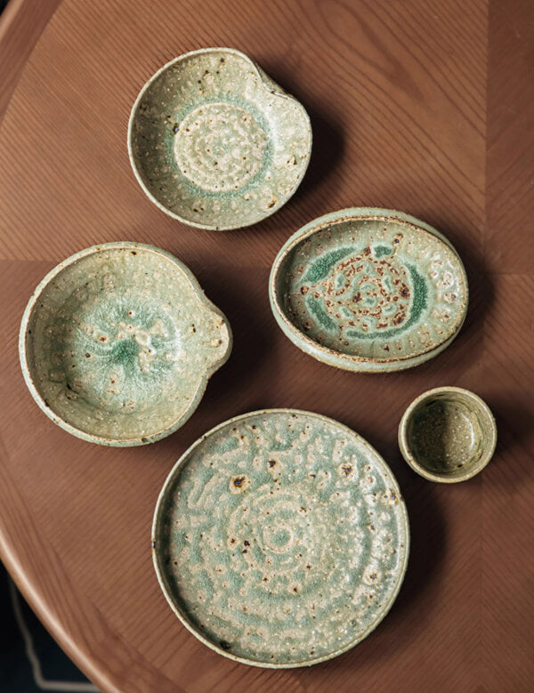 Artisan Green Dinnerware set on a wooden table, featuring textured ceramic dishes in earthy tones.