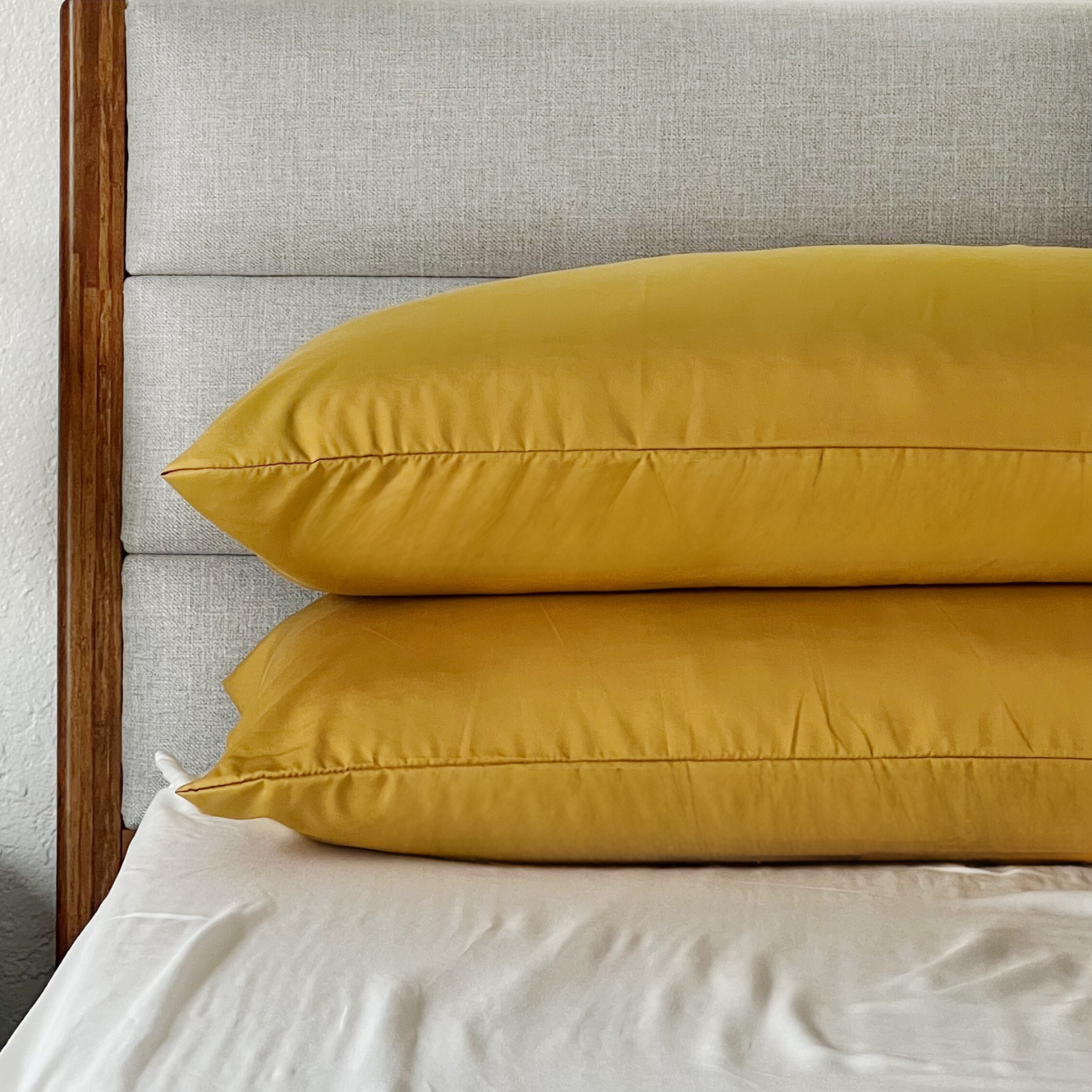 Golden yellow Copper Infused Bamboo Pillowcase Set on a bed with a textured headboard.