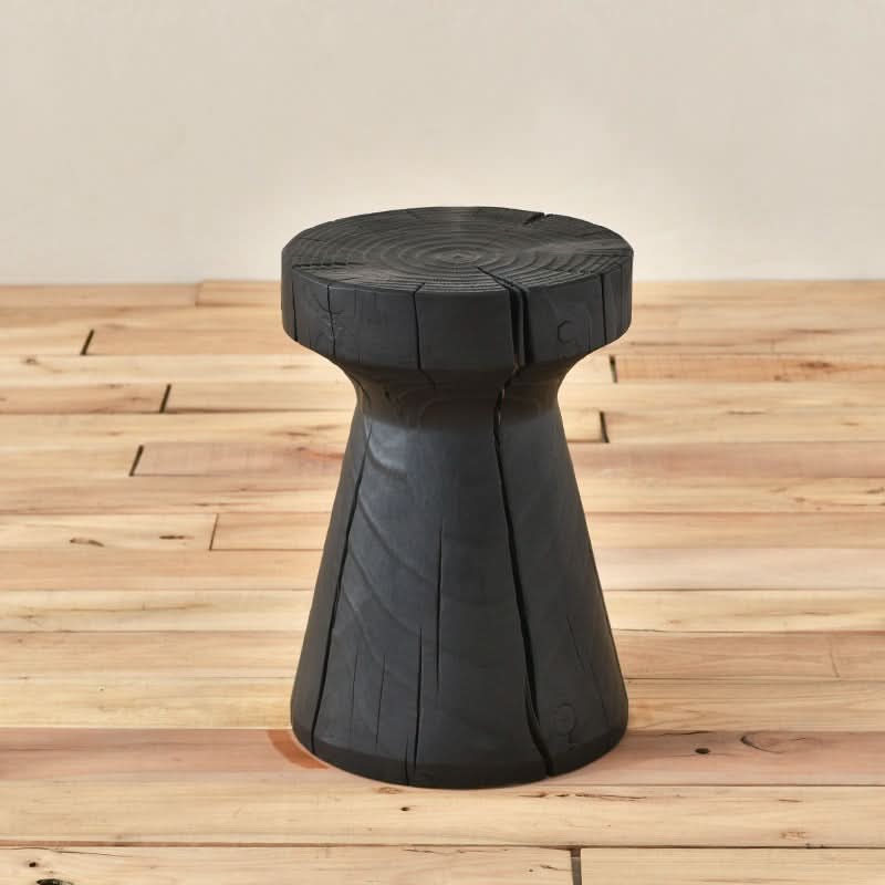 Black wood stool with visible grain and cracks, set on a light wood floor.